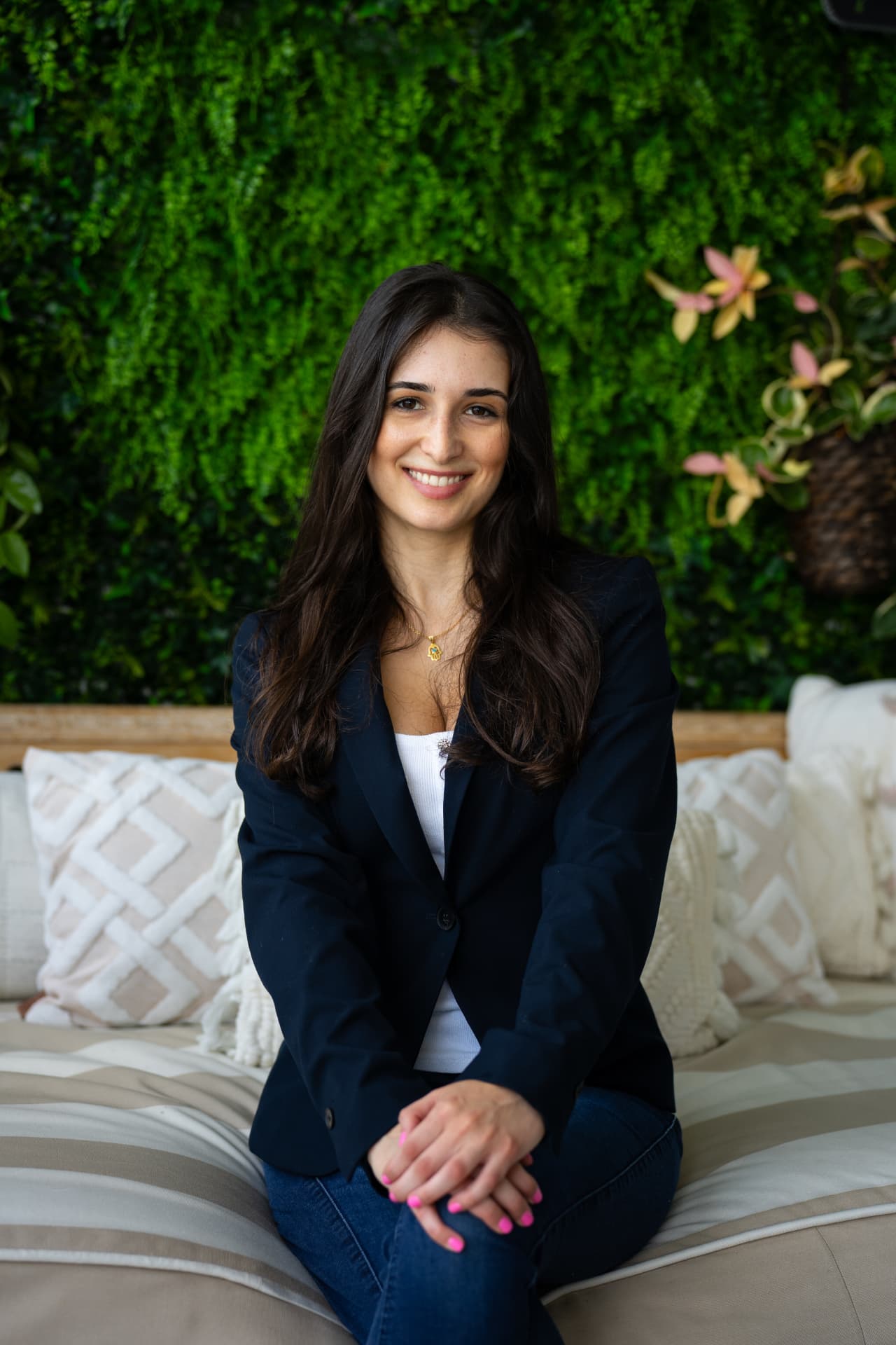 Emily Yagudaev, Registered Mental Health Counselor Intern, smiling in a sunlit space with a green plant wall behind her.